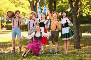 Wall Mural - Young people in traditional German clothes with beer and Bavarian flag celebrating Octoberfest outdoors