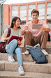 © Jose Calsina - Vertical Two teenagers sitting on the university campus stairs, studying lessons and doing homework using a tablet. Classmates sharing ideas for a project, working with a touchpad. College students