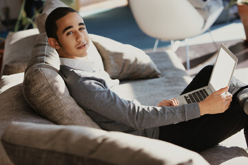 Young man browsing internet on laptop relaxing on couch