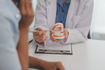 Dentist consultation - patient visit at the dental clinic office. Female dentist wearing dentures to explain teeth Recommend guidelines for orthodontics Dentist giving advice on patient's condition