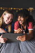 © Wavebreak Media - Happy diverse female friends lying on bed and using tablet at home