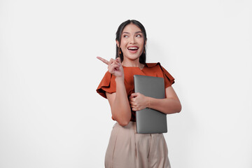 Wall Mural - Confident young Asian woman holding laptop while pointing to the copy space beside her.