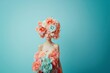 © photolas - A young woman with a large, extravagant floral headpiece covering her head stands against a soft pastel background.