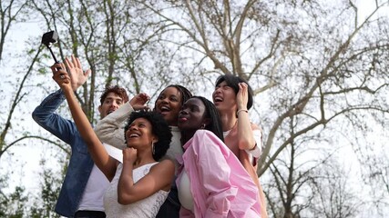 Wall Mural - A group of friends from different ethnic backgrounds taking a playful selfie outdoors in a park. Scene is happy and friendly, as everyone is smiling and enjoying the moment