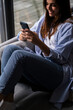 © simona - Smiling adult woman relax sit on sofa at home using cellphone texting chatting with friend, happy young female on couch hold smartphone shop online or check mobile application or social media