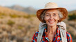 © 29 December - A senior woman in a hat and plaid shirt smiles brightly while hiking in a scenic, natural landscape during a sunny day.