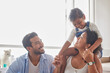 © Alex Shared/peopleimages.com - Couple, girl child and piggyback in home with bonding, fun game and support with love, security and excited. Family, parents and playing with daughter on shoulders in living room for care or activity