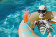 © Alexandra - Skeleton wearing sunglasses relaxing on inflatable ring in swimming pool and holding refreshing cocktail on summer day