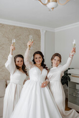 Wall Mural - Three women are celebrating a wedding, with one of them holding a glass of champagne. The bride is wearing a white dress and the other two women are wearing white dresses as well