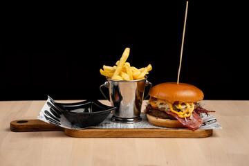 Wall Mural - Gourmet burger with cheese and bacon served with a side of fries on a wooden board