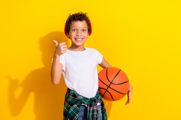 Wall Mural - Photo portrait of adorable little boy hold basketball ball thumb up dressed stylish white garment isolated on yellow color background