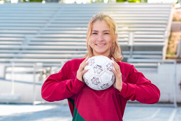 Concepts: sport and outdoor recreation. young soccer player holds the ball on her chest and smiles happily. exercise and active lifestyle