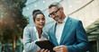 © SneakyPeakPoints/peopleimages.com - Business people, tablet and collaboration outdoor with manager for planning, meeting and travel together. Ceo, woman and technology in city with partnership for research and choice of event location