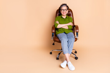 Poster - Full size photo of pretty senior female crossed hands sit armchair wear trendy green outfit isolated on beige color background