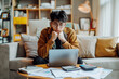 © NoonBusin - Business finance concept. Korean young man sitting on couch looking stressed by calculating expenses from invoices or bills. Calculator and laptop on desk. No money to pay mortgage or loan.