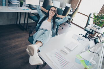 Wall Mural - Photo of smiling positive lady accountant dressed denim jacket arms behind head dreaming indoors workplace workstation loft