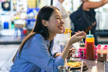 Young Asian woman traveler tourist eating Thai street food in China town night market in Bangkok in Thailand - people traveling enjoying food culture concept