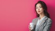© siripimon2525 - Close-up of a Japanese businesswoman holding a cup of coffee and looking relaxed, wearing a grey blazer and white blouse, standing in front of a bright pink background, Portrait half-body,