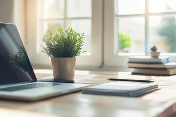 Poster - A close-up view of a wooden desk in a bright office corner, featuring a laptop, a potted plant, and a closed notebook