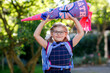 © Irina Schmidt - little girl with glasses and a blue backpack, dressed in a navy uniform, holds a colorful school cone called Schultuete and backpack. Happy child smiling, ready for her first day of school