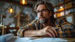 © svastix - A mature man with glasses and wavy hair, sitting at his drawing desk with architectural plans, deep in thought. The warm, ambient lighting adds a sense of devotion.