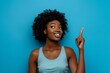 © Elmira - A young woman with an afro hairstyle stands against a blue background and points upward with a smile