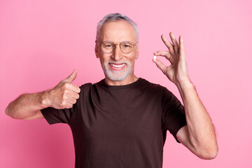 Poster - Portrait of positive man with beard dressed brown t-shirt in glasses hold pills showing thumb up isolated on pink color background