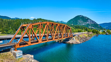 Wall Mural - Aerial View of Rust-Colored Truss Bridge Over Blue River with Mountain Backdrop