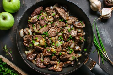 Wall Mural - Close up top view of German dish fried beef liver with green apples and onions in a pan on the table