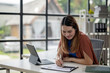 © Wasana - A woman is sitting at a desk with a laptop and a piece of paper