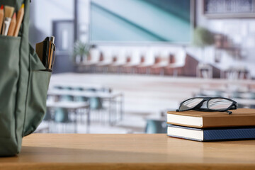 Back to school concept. Wooden desk top with backpack and apple and school stuff with blurred classroom backround 