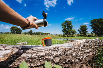 Wall Mural - pour tea from a thermos into a mug in nature, a hot drink, metal tourist utensils for trekking.