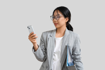 Sticker - Happy young Asian businesswoman with folder and mobile phone on grey background