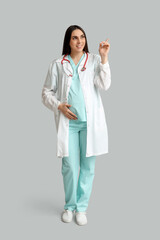 Poster - Beautiful young pregnant doctor pointing at something on grey background