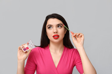 Sticker - Beautiful young woman with palette of eyeshadows and makeup brush on grey background