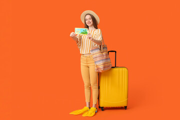 Sticker - Smiling young woman with suitcase and flippers showing gift voucher on orange background. Travel concept