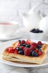 Wall Mural - Tasty puff pastries with berries and tea on white marble table, closeup