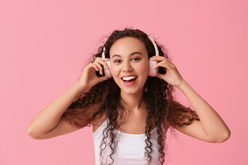 Wall Mural - Happy young African-American woman in headphones on pink background