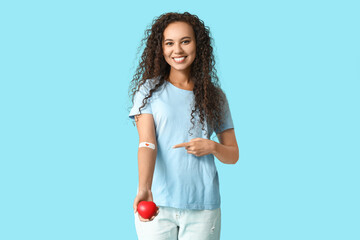 young female african-american blood donor with heart pointing at applied medical patch on blue backg