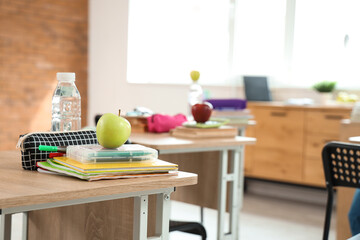 Canvas Print - Apple with school stationery on desk in classroom, closeup