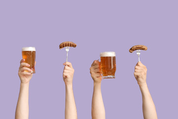 Hands with glasses of beer and sausages on lilac background