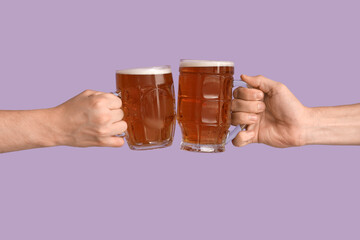 Hands with mugs of beer on lilac background