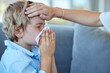 © Delcio Fernandes/peopleimages.com - Blowing nose, child and hand of mother for fever with flu, cold or allergy on sofa at home. Sick, medical emergency and mom feel head of kid for high temperature with illness in living room at house.
