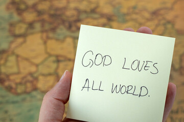 Wall Mural - God loves all world, hand holding  handwritten inspirational quote with ancient map in the background. Close-up. Christian biblical concept of Jesus Christ's grace, mercy, forgiveness, and care.