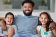© peopleimages.com - Happy portrait, father and children on couch for healthy relationship, bonding time and care in home. Smile, papa and kids with love hug for support, trust and peace or relax together in living room