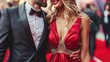 © tashechka - Close-up of a stylish couple dressed in a tuxedo and red gown, smiling at a glamorous red carpet event.