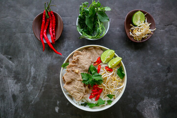 Wall Mural - A Bowl Pho Bo traditional Soup with beef, rice noodles, ginger, lime, chili pepper in bowl. Close up. Vietnamese cuisine served on black background