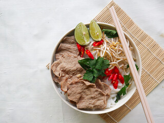 Wall Mural - A Bowl Pho Bo traditional Soup with beef, rice noodles, ginger, lime, chili pepper in bowl. Close up. Vietnamese cuisine served on black background