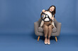 © comzeal - Young Asian businesswoman sitting on armchair and holding the steering wheel of a car isolated on blue studio background