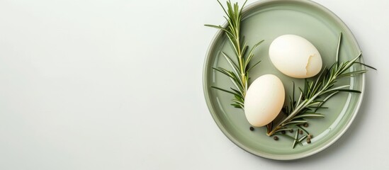 Aufkleber - Overhead shot of two boiled eggs and fresh rosemary on a green plate against a white background, serving as a festive Easter holiday decoration with ample copy space image.